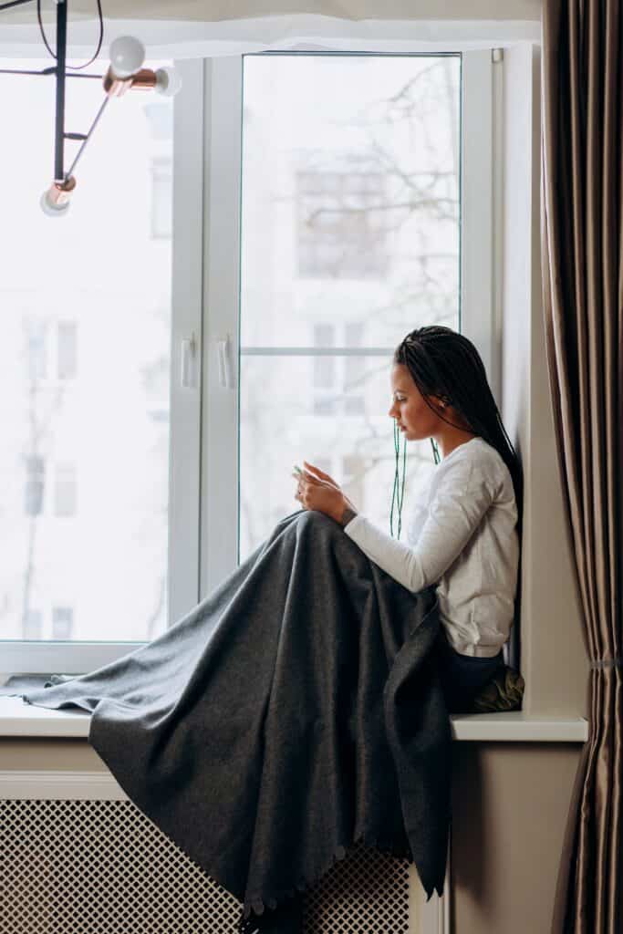 Vrouw zit bij het raam met deken